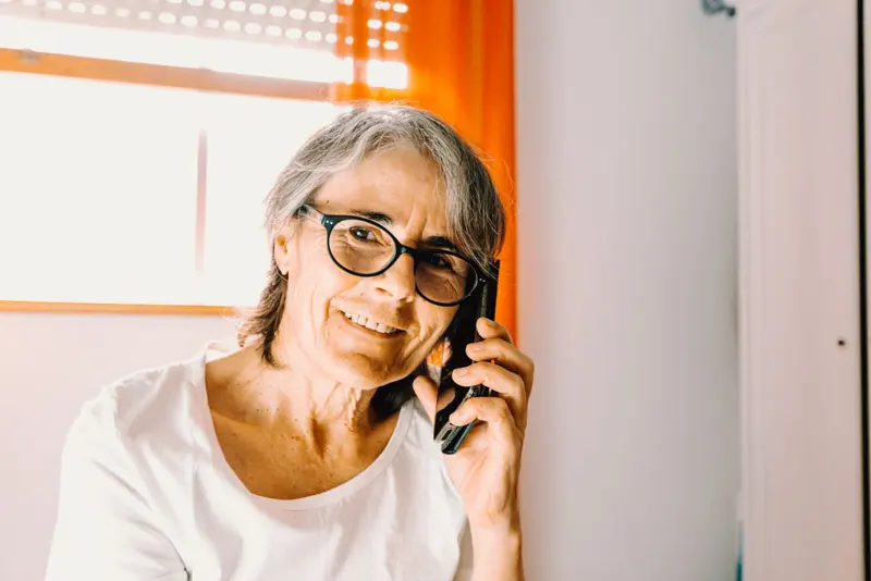 Una signora con gli occhiali sorride mentre parla al telefono.